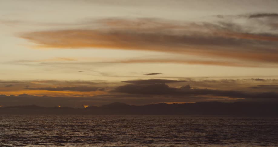 A distant mountain range and the ocean are seen under a sunset sky