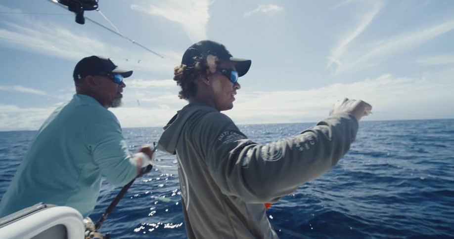 Two fishermen pulling a line while on a boat in the middle of the ocean