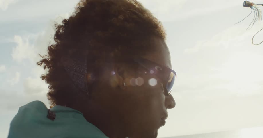 Close up of a person with curly hair wearing sunglasses on a windy sunny day