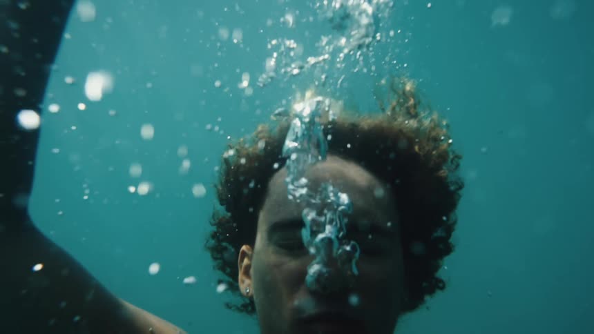 Man underwater in ocean descending as oxygen bubbles rise