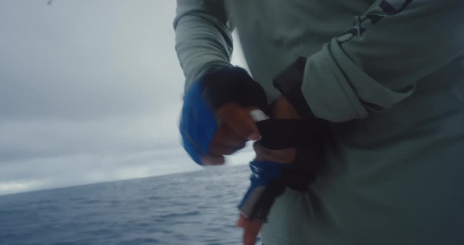 Young man puts on gloves while standing in a moving boat on a windy day