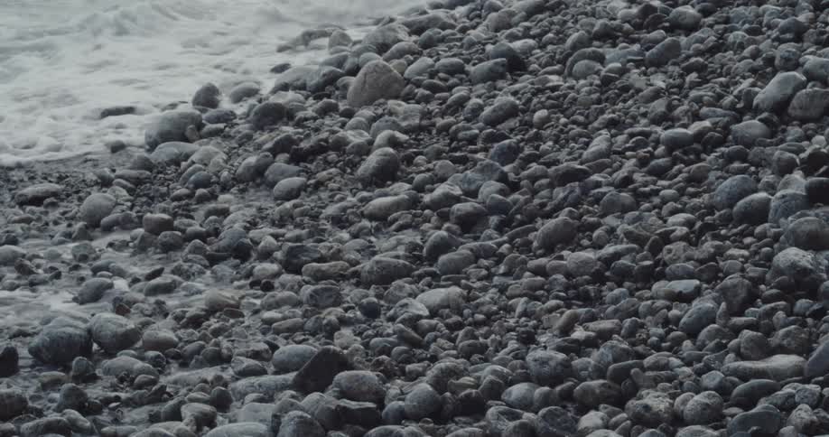 Waves foam while flowing onto a pebble covered shore