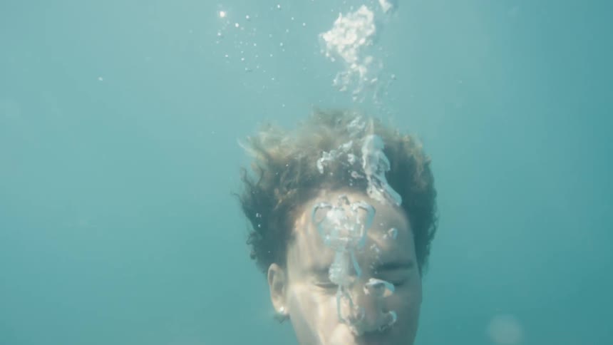 Man diving with eyes closed and oxygen bubbles and coming up