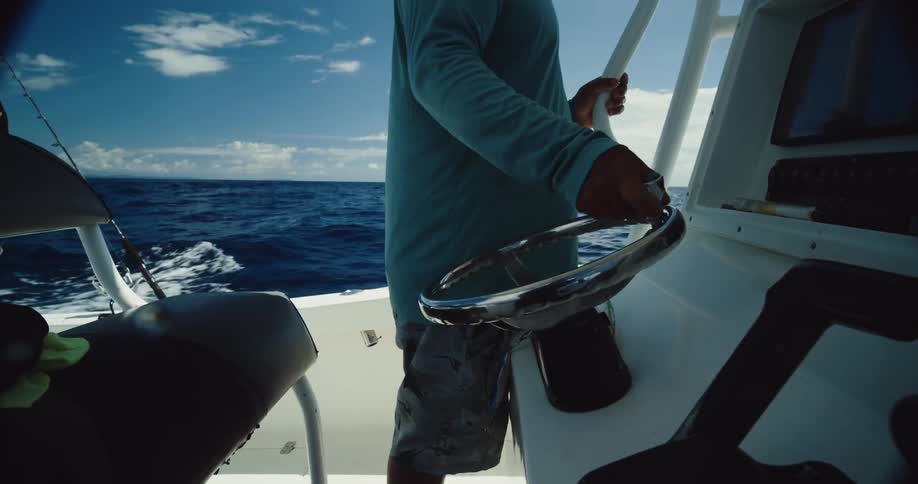 A person is steering a boat on the open ocean with a clear blue sky and scattered clouds in the background
