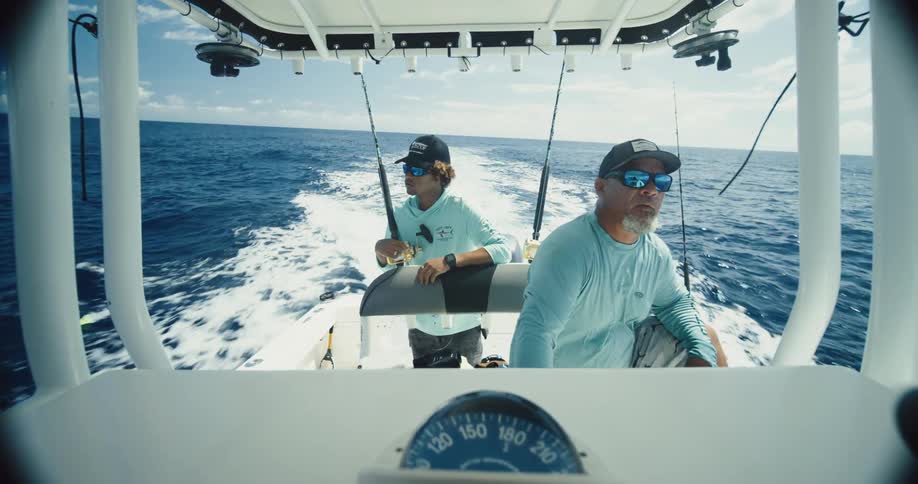 Two fishermen in caps on a boat moving through the sea