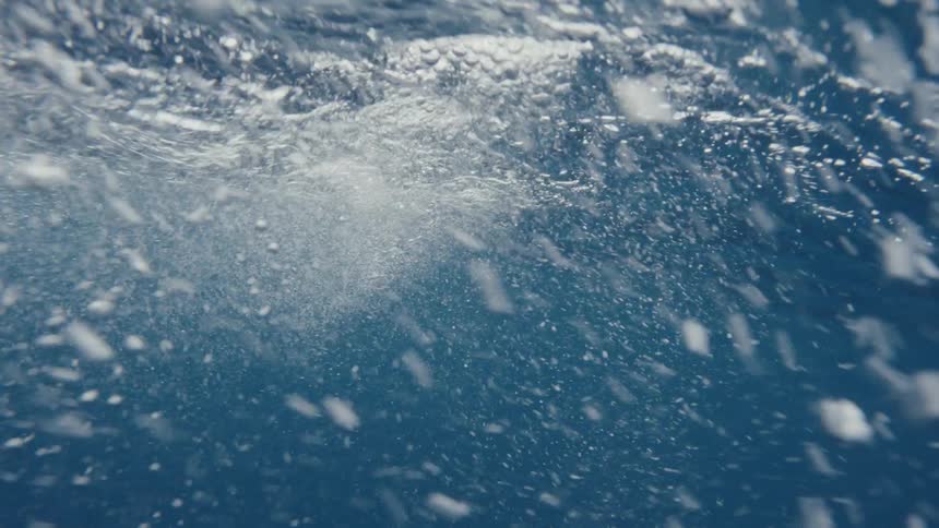 A view of the ocean with several waves and several white bubbles underwater