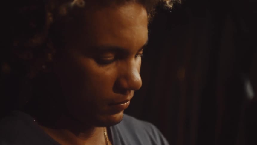 The face of a man with brown skin and yellow hair is passing a wire through an orange circular object