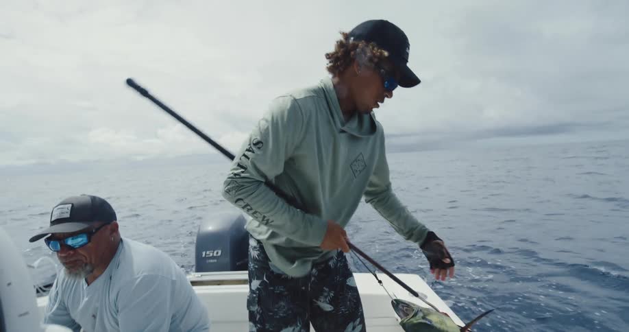A person on a boat is holding a harpoon and has caught a fish