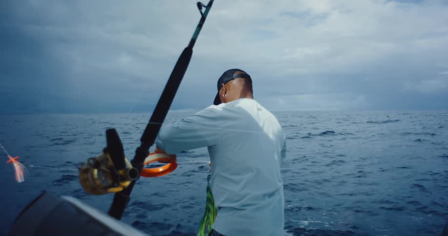 Man manipulates a fishing line and a large lure while in a boat on the sea on an overcast day