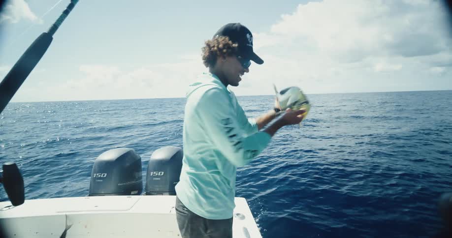 A person on a boat is holding a freshly caught fish over the side of the boat