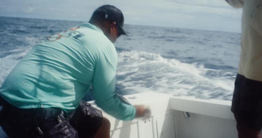 Two men fishing on a boat release a fish back into the ocean