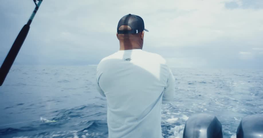 A person on a boat is holding an orange ring while facing the ocean with fishing equipment visible in the background