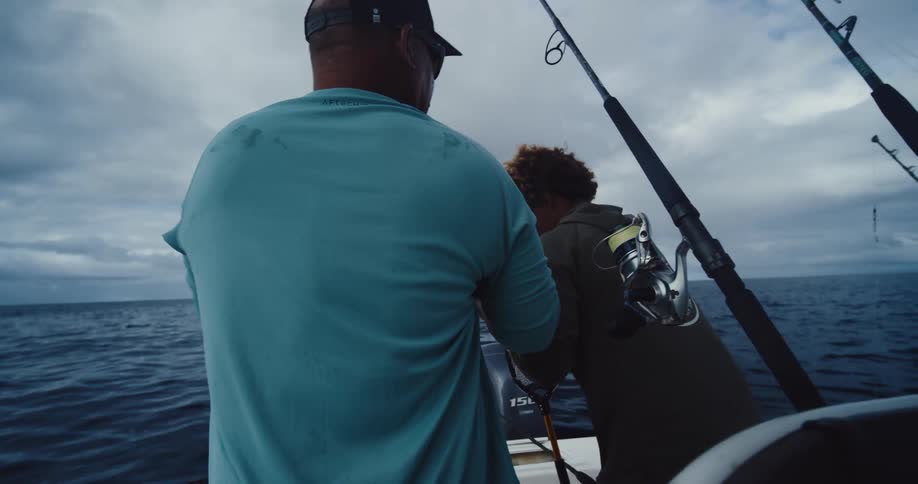 A couple of men are fishing on a boat in the ocean under a cloudy sky