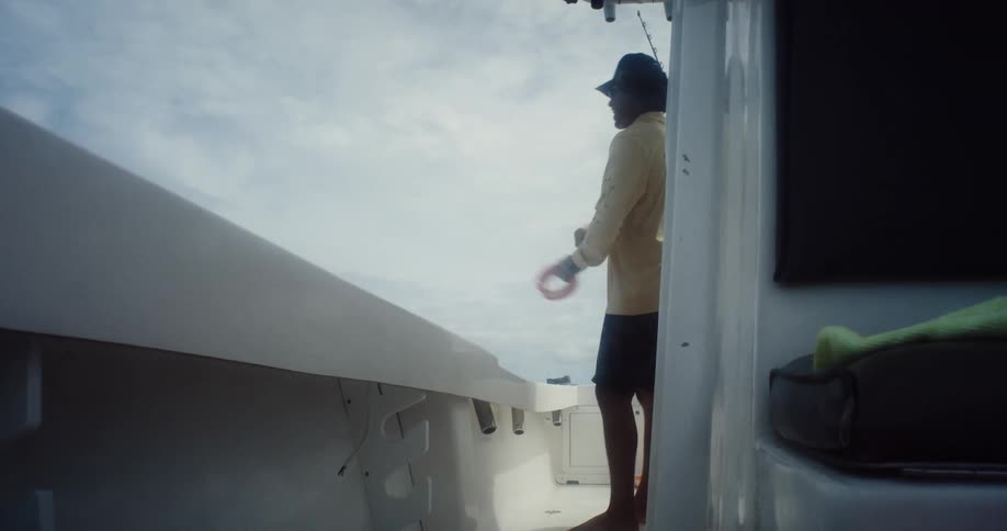 A person is standing barefoot on a boat holding a fishing line and casting it into the ocean