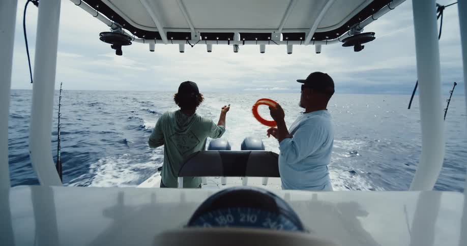 Two fishermen reeling in an orange line while on a boat moving through the sea