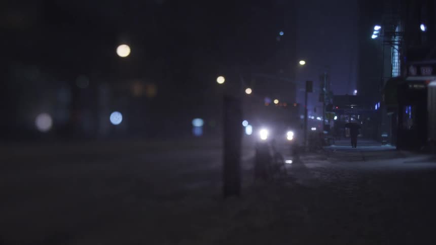Snow falls in a city at night