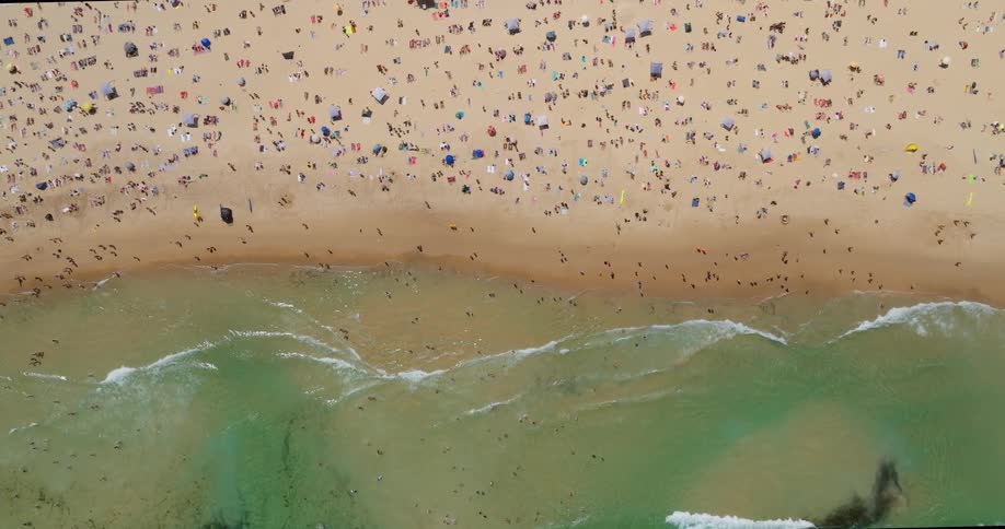 Aerial of waves rolling onto a busy beach on a summer day