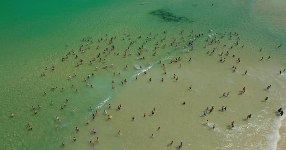 A crowded beach with people swimming and sunbathing in the shallow water