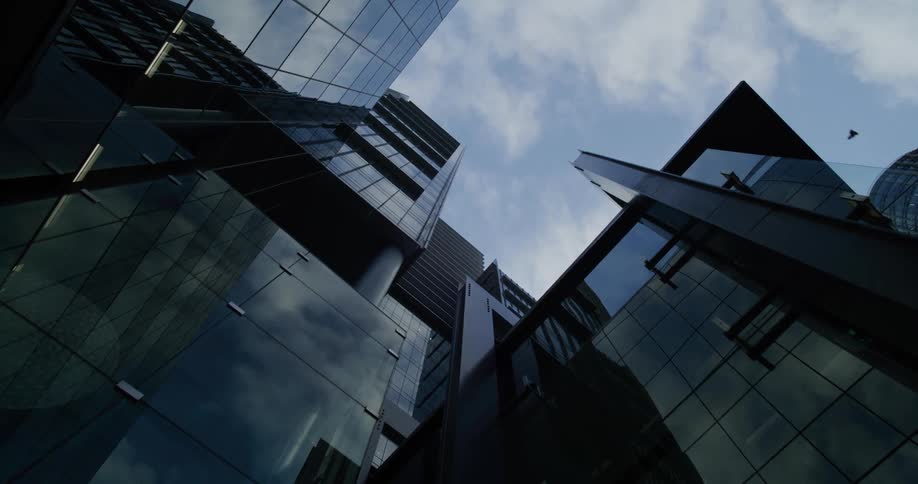 An upward view of modern skyscrapers with reflective glass facades against a partly cloudy sky