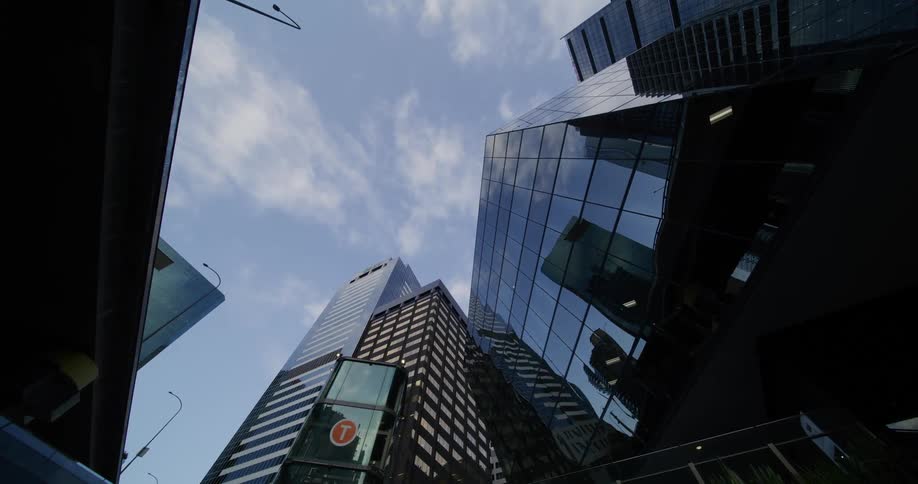 An upward view of modern skyscrapers with reflective glass facades against a partly cloudy sky