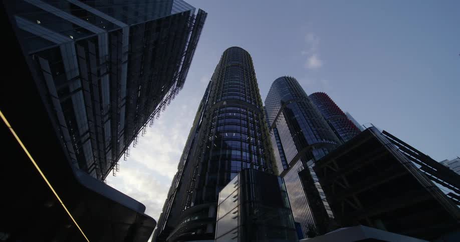 An upward view of modern skyscrapers with reflective glass facades against a partly cloudy sky
