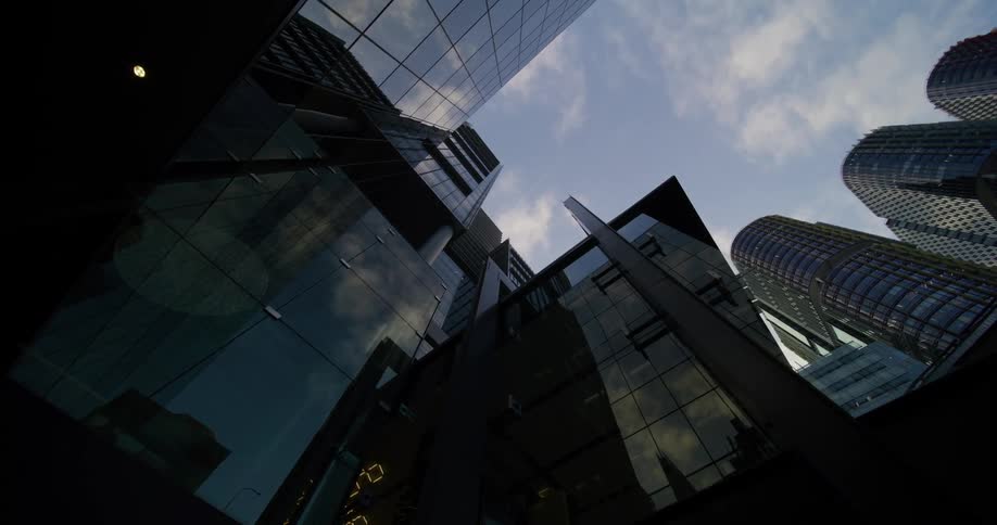 An upward view of modern skyscrapers with reflective glass facades against a partly cloudy sky