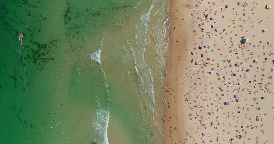 Aerial view of a crowd of bathers enjoying a beach with clear greenish waters