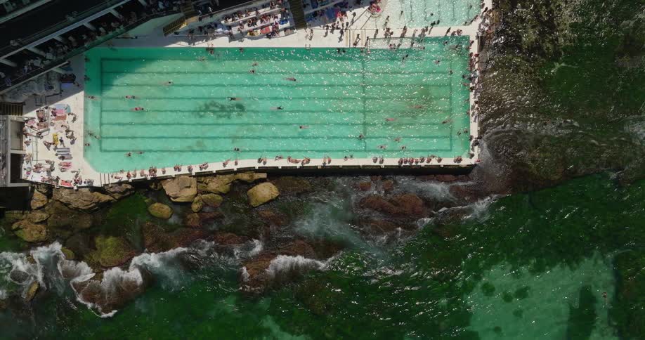 Aerial view of a beachfront swimming pool with crystal clear waters packed with swimmers