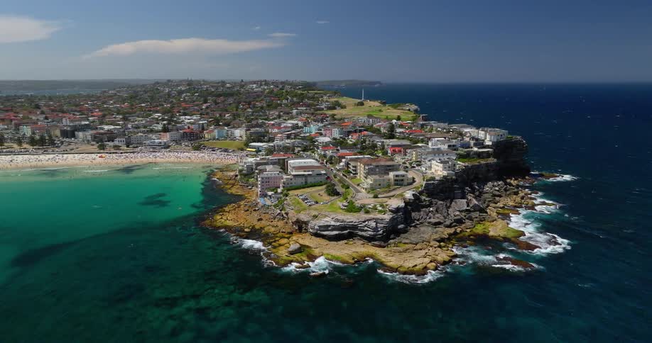 Aerial view of a stunning coastline with crystal clear waters in shades of green and blue contrasting with rock formations and a colorful seaside village