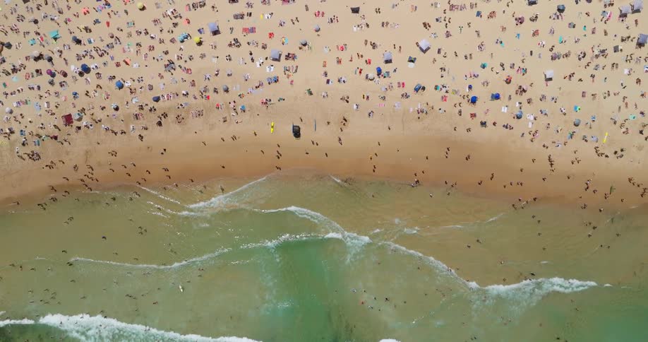 Birds eye view of a crowded beach with people sunbathing and swimming