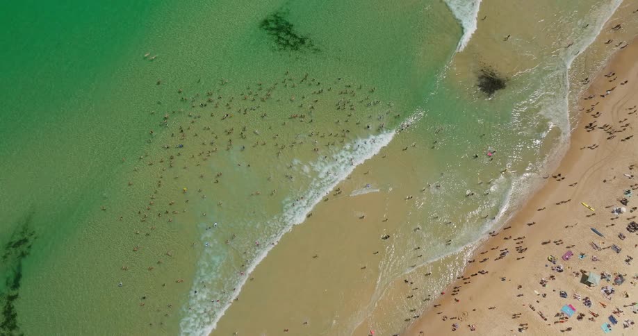 A sandy beach crowded with people swimming in clear turquoise water and relaxing on the shore