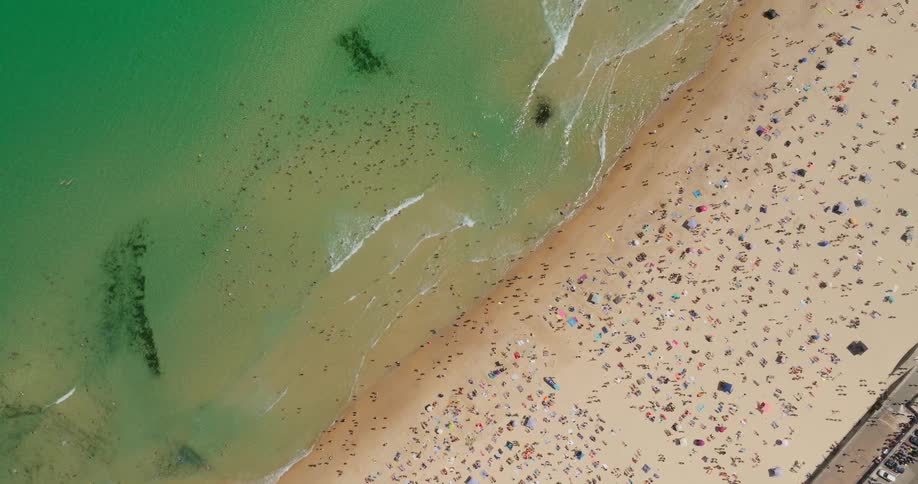 Aerial of a crowded beach with people swimming and sitting on the sand