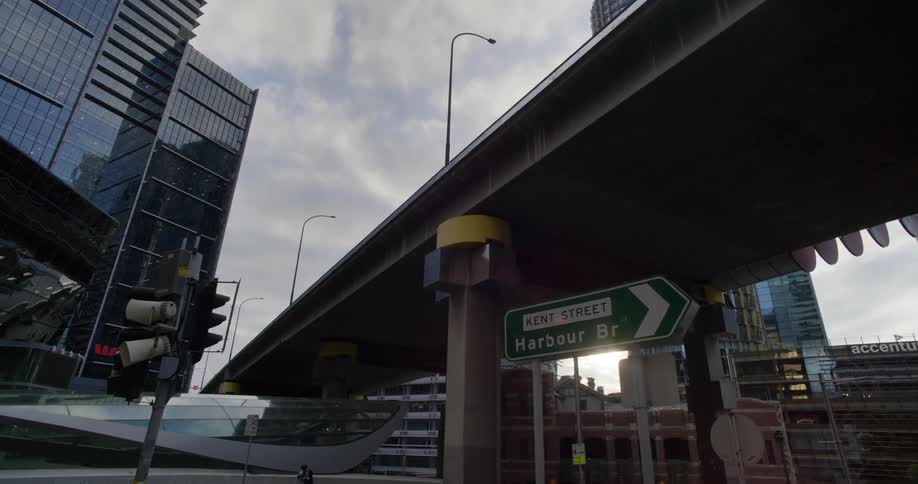 An overpass that passes through a city and on the ground there are several signs and a traffic light and some buildings on the sides