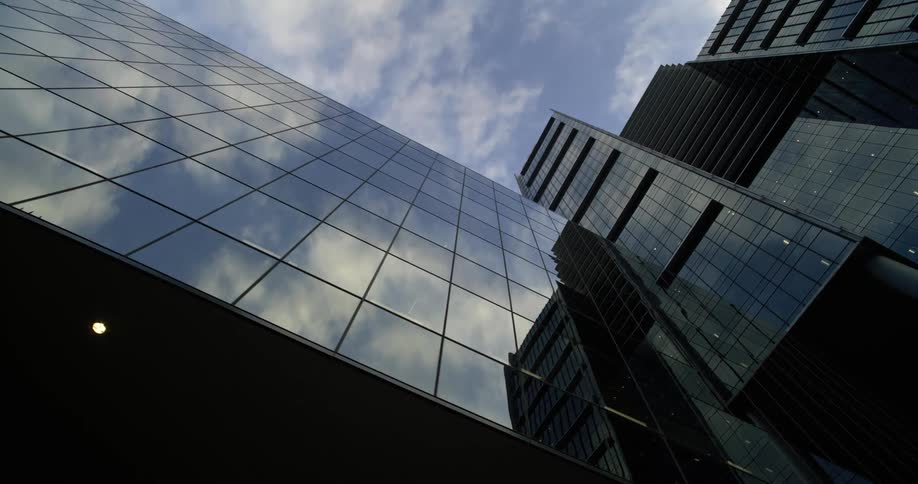 A tall modern building with a glass facade reflecting the sky and clouds