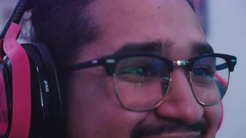 Man wearing headphones and eyeglasses breaks into a big smile while watching a large screen