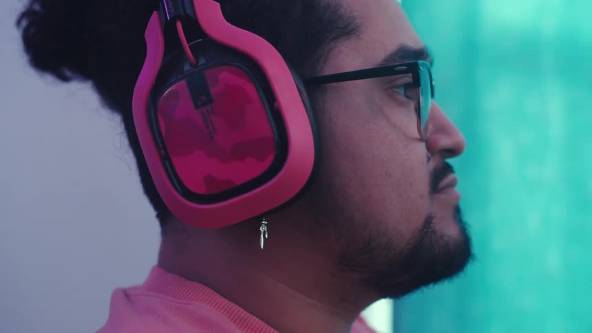 A person is wearing pink overear headphones set against a background with teal lighting