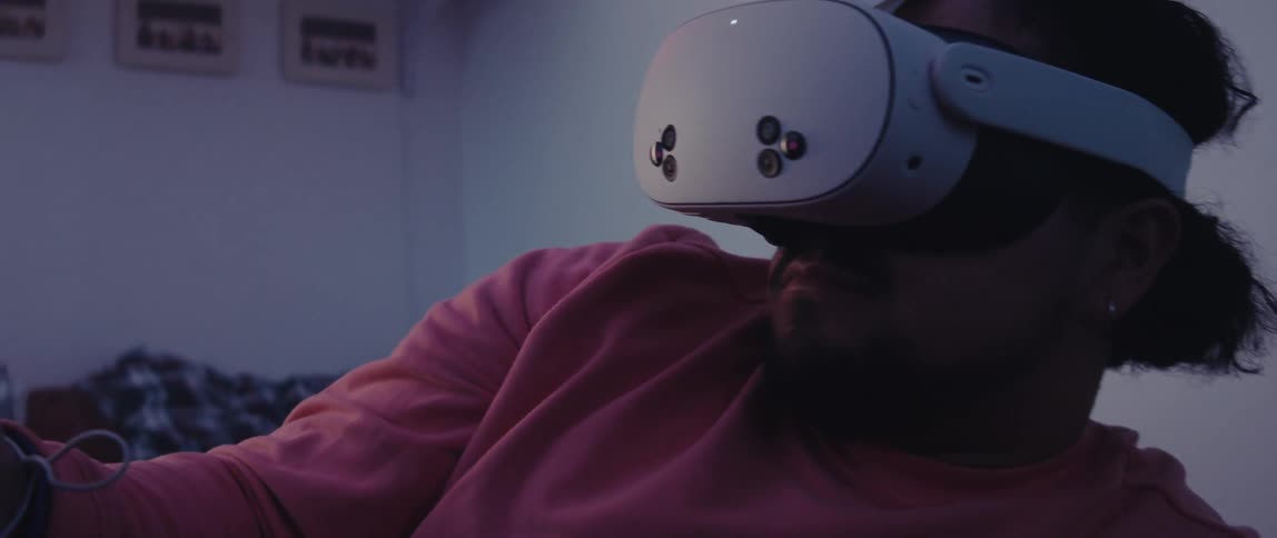 Man leans back on his bed and interacts with virtual reality using a headset and a controller