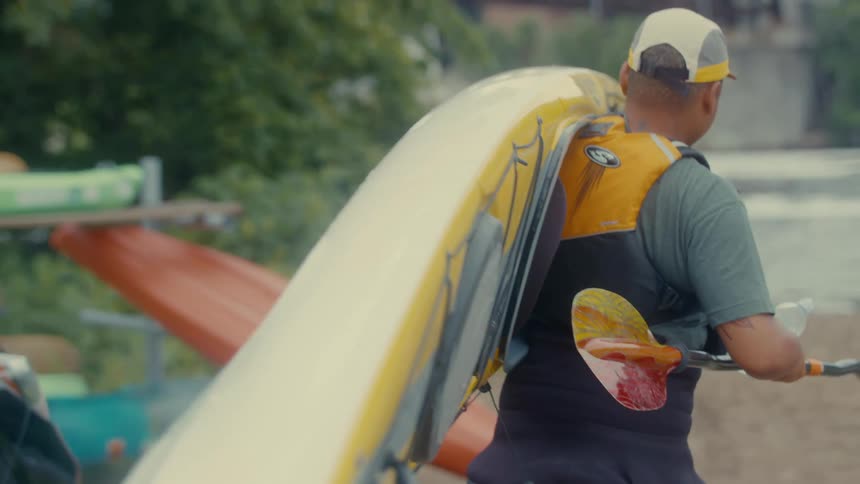 Man carrying a kayak over his shoulder towards the river