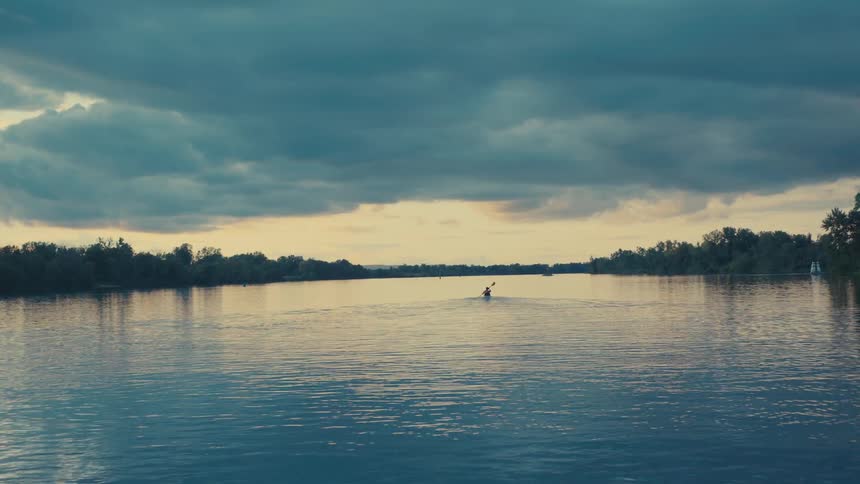 A person is kayaking on a calm body of water using a doublebladed paddle to propel a yellow kayak forward