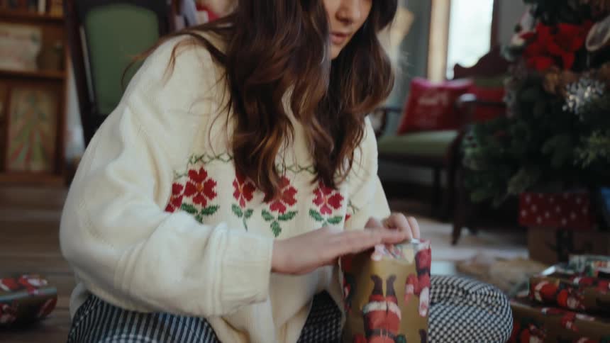 Woman sitting in living room wrapping a christmas present