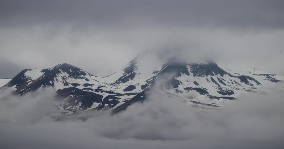 The tops of snow covered mountains are peeking out from a thick layer of clouds