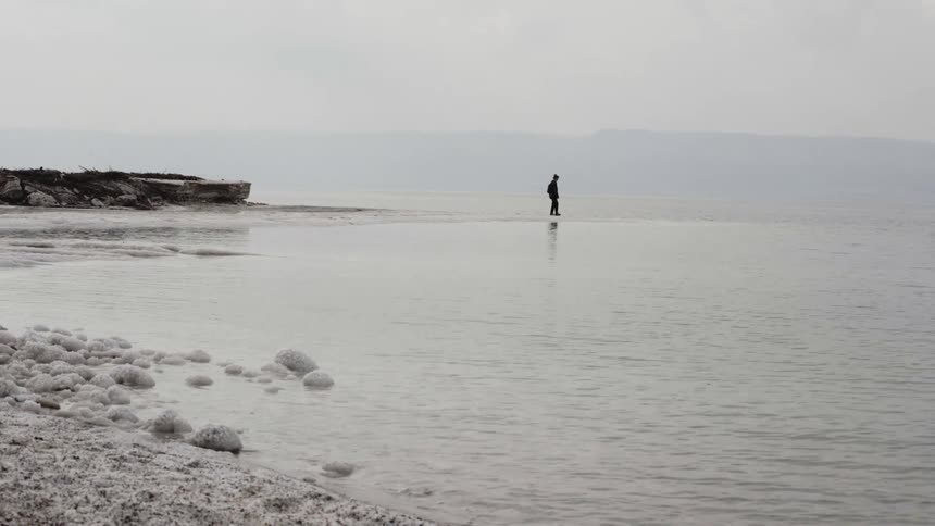 Person walking on a lake with mountains in the background
