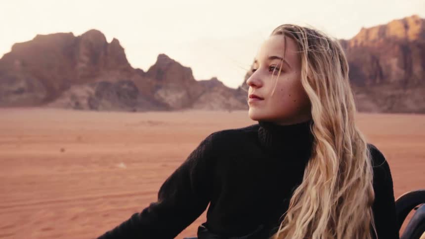 Woman sitting in an open vehicle moving through a desert region with canyons in the background