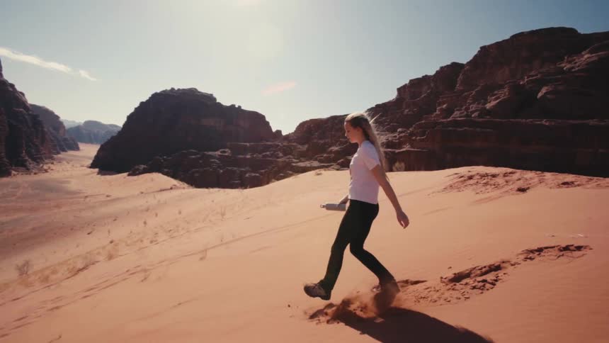Woman descending a desert dune with canyons around
