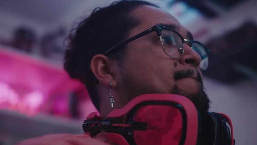 A man with headphones around his neck sits in a room and stares at something