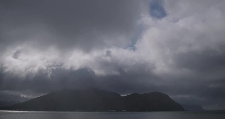 A dramatic sky filled with dark swirling clouds looms over a calm body of water and distant mountains