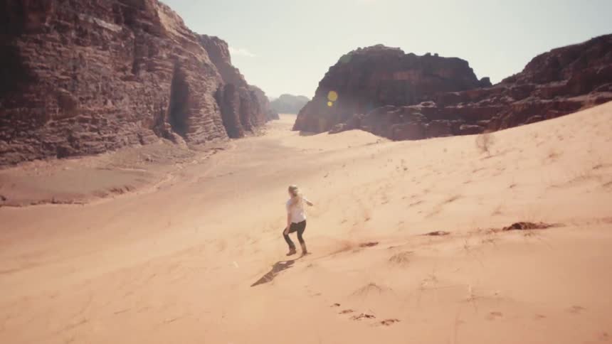 Woman running down a desert area with canyons around