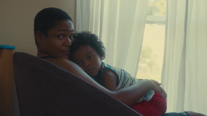 Mother cuddles her child while sitting at home in a chair near the window