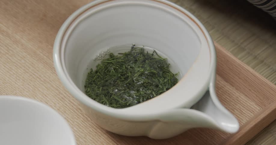 Hot water is being poured over loose tea leaves in a small bowl