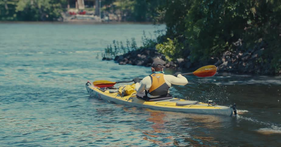 A person is kayaking on a calm body of water using a doublebladed paddle to propel a yellow kayak forward